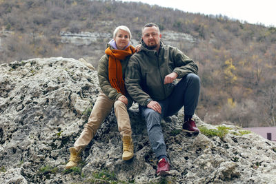 Man and a woman are sitting on a rock in autumn in warm clothes