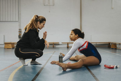 Female coach training teenage girl to do warm up exercise at gym