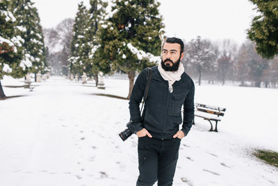 Handsome man with camera standing on snow covered footpath during winter