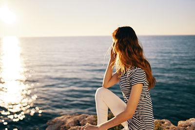 Rear view of woman at sea shore against sky during sunset