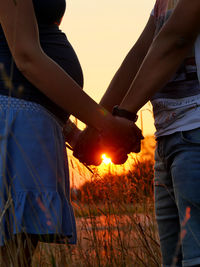 Midsection of man holding hands against sky at sunset