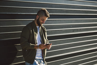 Smiling man standing in front of facade lookiung at cell phone