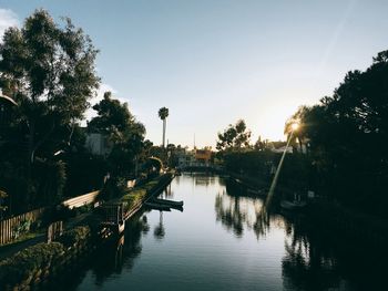 Canal amidst trees against sky during sunset