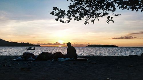 Silhouette people on beach against sky during sunset