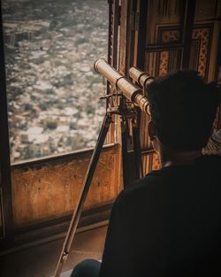 Rear view of man looking through telescope