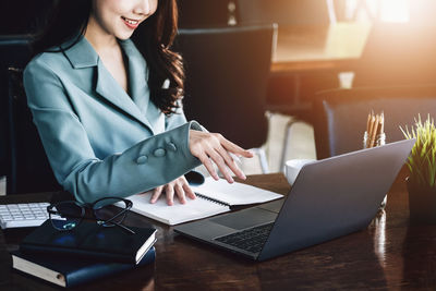 Midsection of businesswoman using laptop at table