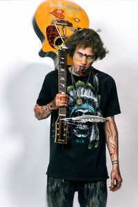 Portrait of man with face paint holding guitar against wall at home