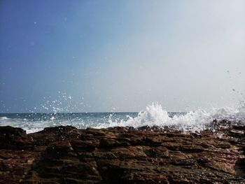 Waves splashing on rocks at shore against sky