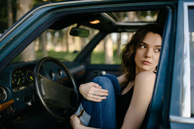Young hipster woman looking in the forest from vintage car
