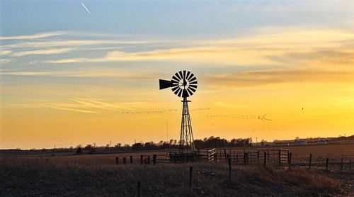 Traditional windmill on field against sky during sunset