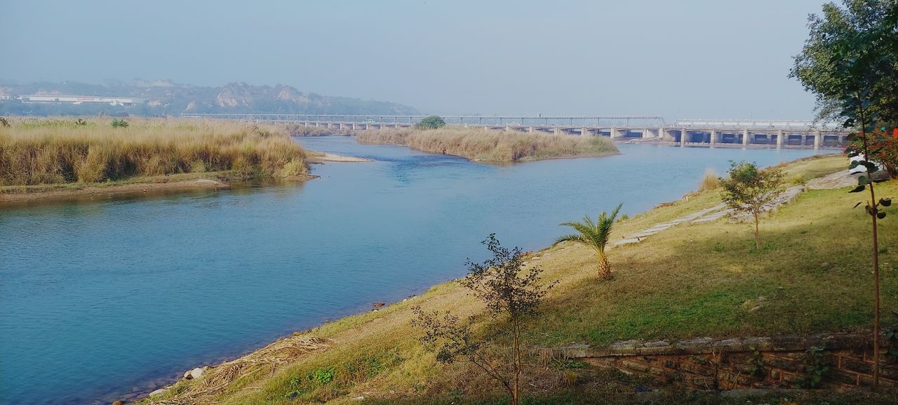 water, reservoir, body of water, plant, sky, nature, scenics - nature, river, tree, beauty in nature, land, shore, tranquility, day, beach, tranquil scene, no people, travel destinations, clear sky, environment, landscape, coast, grass, architecture, outdoors, travel, tourism, non-urban scene, built structure, reflection, blue