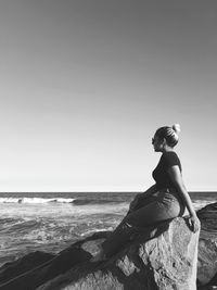 Woman sitting on rock at beach against clear sky