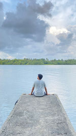 Rear view of man sitting on lake against sky