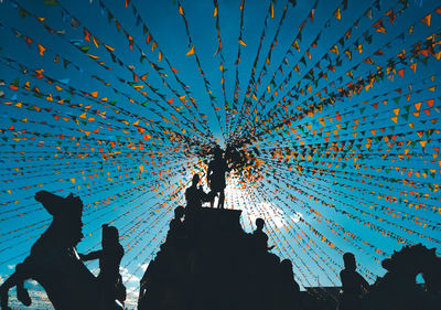 Low angle view of silhouette statues and buntings against sky during sunny day