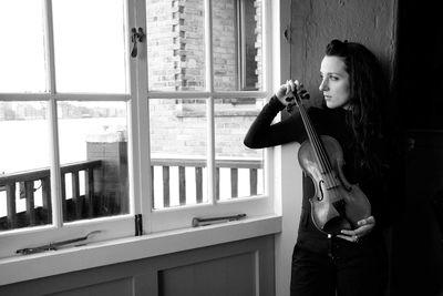 Woman holding violin by window at home