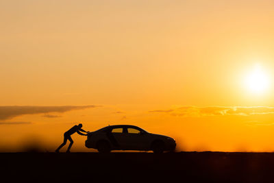  silhouette of man driver pushing his car along on an empty road after breakdown at sunset,