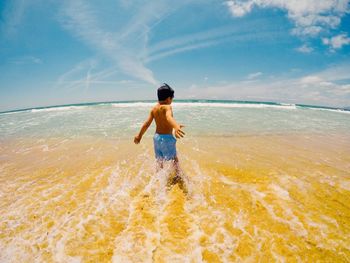 Shirtless boy enjoying at beach against sky during sunny day