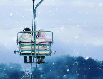 Rear view of ski lift against sky during winter