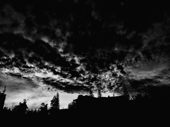 Low angle view of silhouette trees against storm clouds