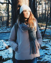 Portrait of woman standing by tree in forest during winter