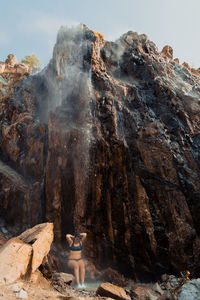 Woman sits beneath hot waterfall in idaho enjoying the warmth during a cold early morning