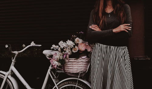 Midsection of woman standing by bicycle and flowers in city