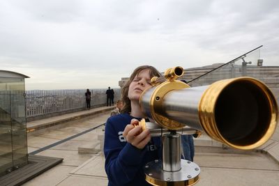 Boy looking through coin-operated binocular against sky