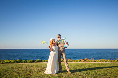 Woman holding umbrella by sea against clear blue sky