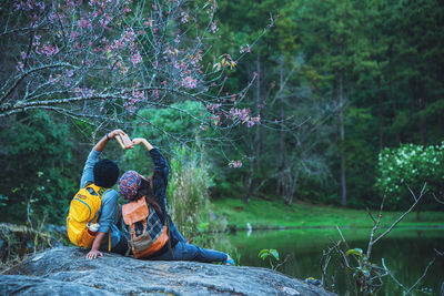 Rear view of couple sitting by lake on rock at forest