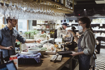 Male customer placing order to female owner at delicatessen store during covid-19