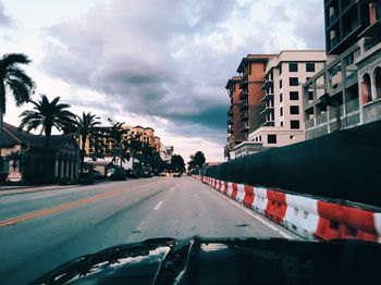 Road passing through city against cloudy sky