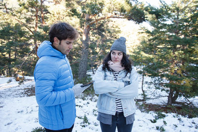 Man using mobile phone by angry woman while standing on snow covered field