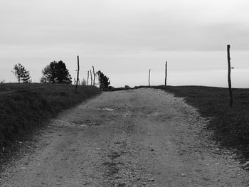 Dirt road amidst field against sky