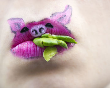 Close-up of lips with pig painting biting leaves