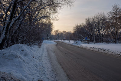 Snow covered road against sky during sunset