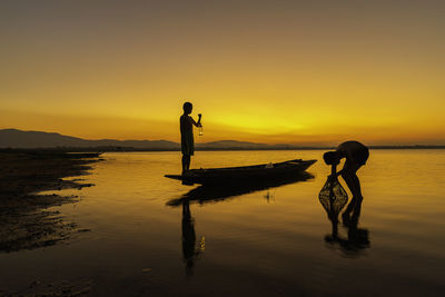 Silhouette people standing on lake against sky during sunset