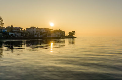 Scenic view of sea by buildings against sky during sunset