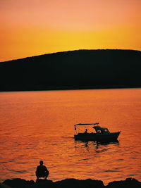 Silhouette people on boat in sea against orange sky