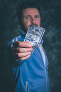 Portrait of man holding american one hundred dollar bill against wall