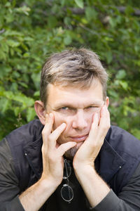 Portrait of man with head in hands sitting against plants