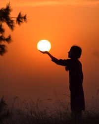 Optical illusion of silhouette woman holding sun against sky during sunset