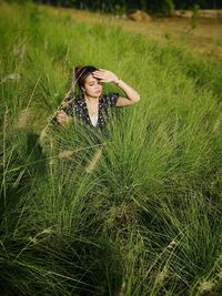 Woman shielding eyes while sitting on grassy land