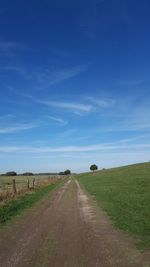 Empty road amidst field against blue sky