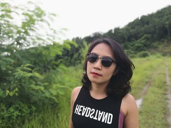 Portrait of young woman wearing sunglasses standing against trees