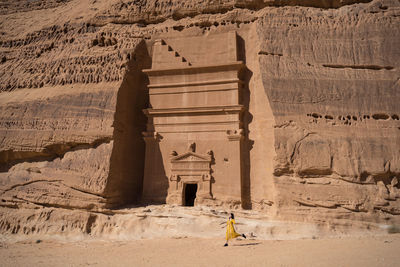 Happy woman traveler walking near tombs carved into cliffs in madain saleh in saudi arabia