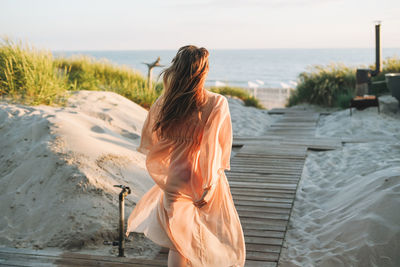 Rear view of woman with arms raised standing at beach