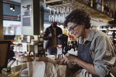 Female owner packing order in paper bag at delicatessen shop