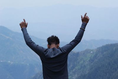 Rear view of man with arms raised standing by mountains against sky