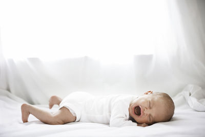 Side view of baby girl crying while lying on bed at home