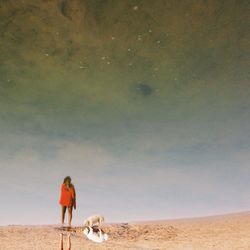 Woman and dog reflecting in water at beach